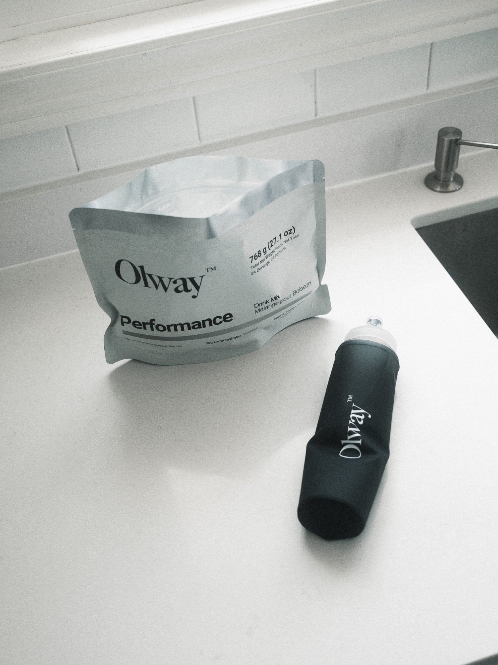 Performance Drink Mix pouch beside a rolled Olway Hydration Flask 500ml on a kitchen counter