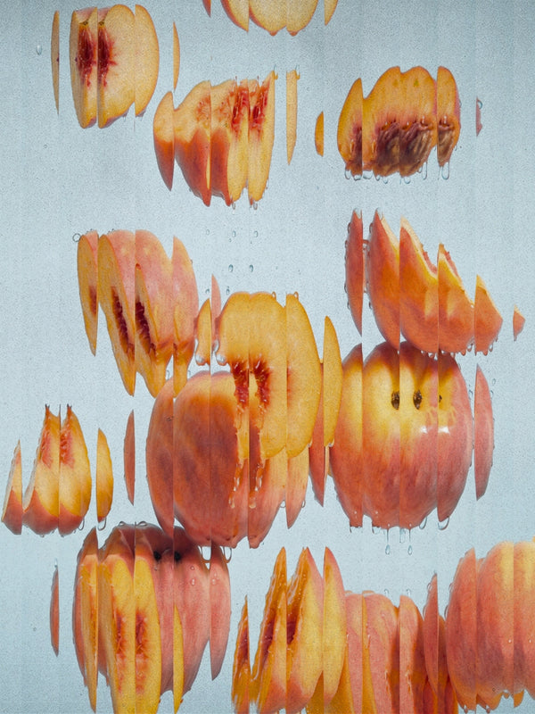 Abstract photographic print of sliced and whole Peach Salt in water against a pale blue-gray background, with reflections and droplets visible.